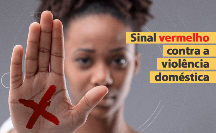 Imagem de uma mulher negra mostrando a palma da mão com um X vermelho desenhado no centro e o texto "Sinal vermelho contra a violência doméstica"