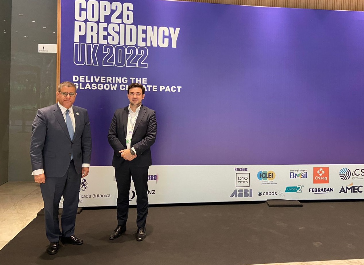 Alok Sharma e Vicente Loiácono Neto, em pé em frente ao painel do evento