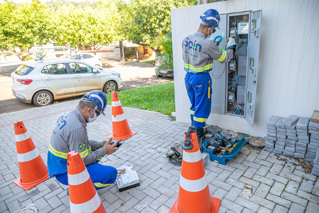Dois homens uniformizados instalando novo medidor inteligente em quadro de energia de residência