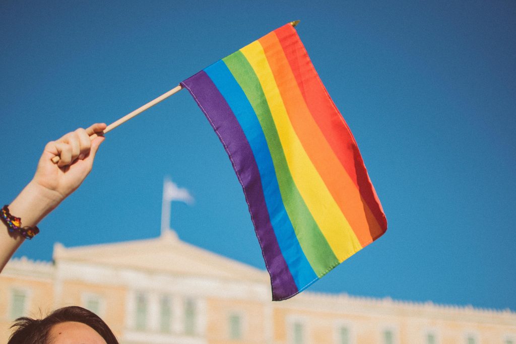 A mão de uma pessoa branca segura uma bandeira colorida LGBTI+
