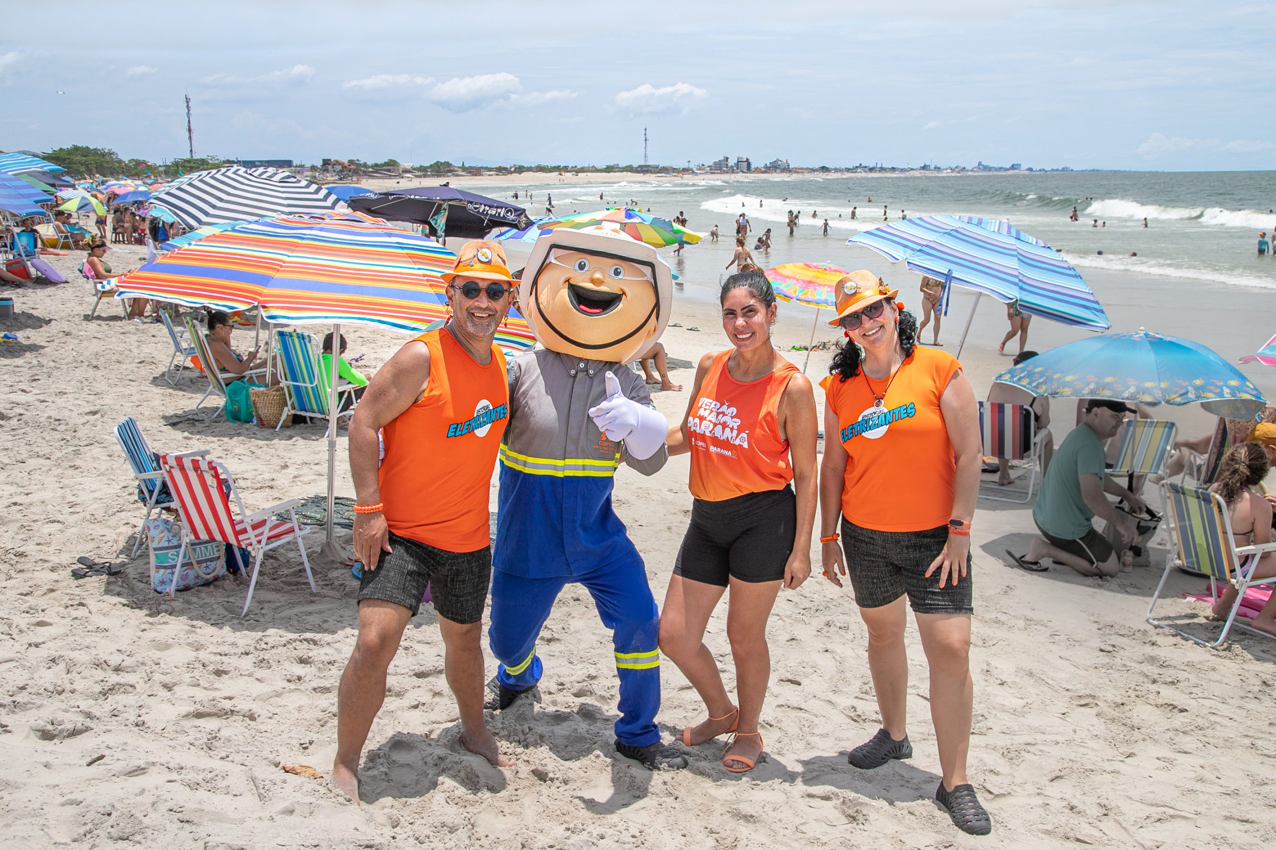 Quatro pessoas na areia da praia, com guarda-sóis ao fundo