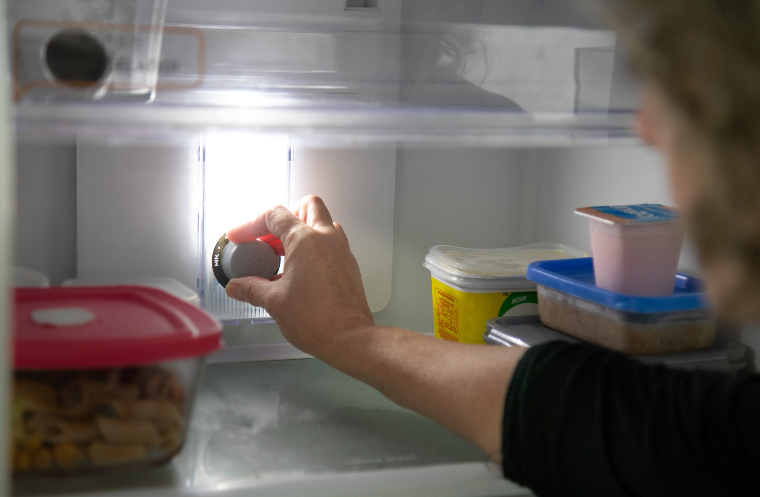 Parte interna da geladeira; mão toca o botão que regula temperatura
