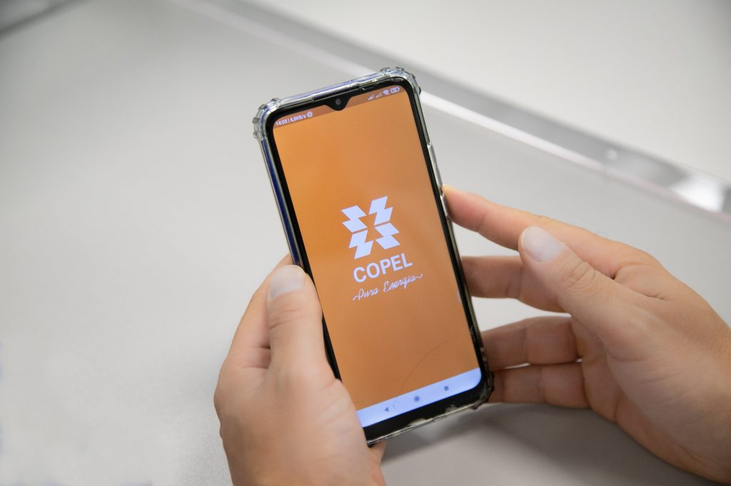 Mãos seguram celular com o aplicativo da Copel sobre uma mesa