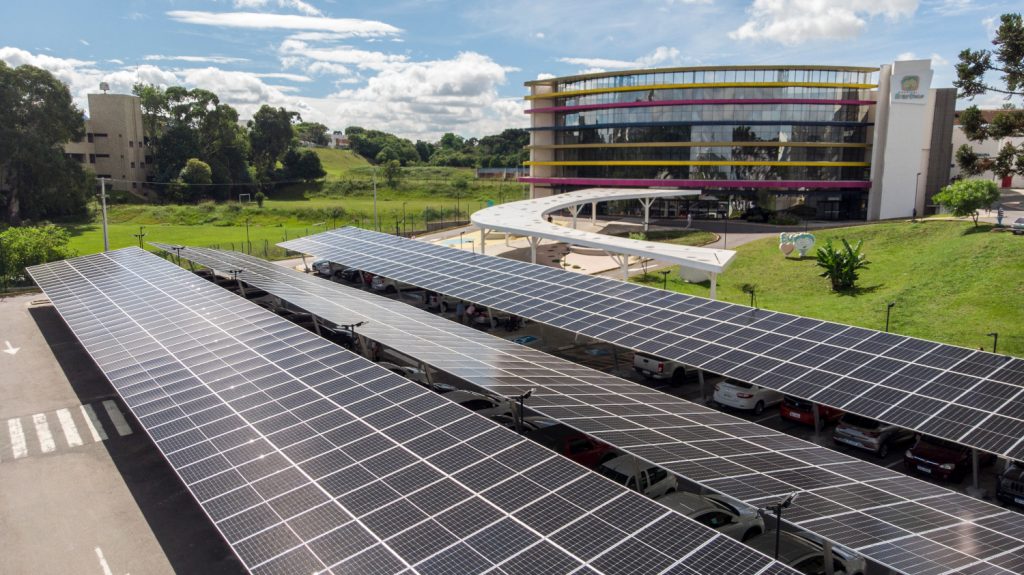 Vista aérea de placas de geração solar em frente ao prédio do hospital que tem detalhes coloridos na fachada circular