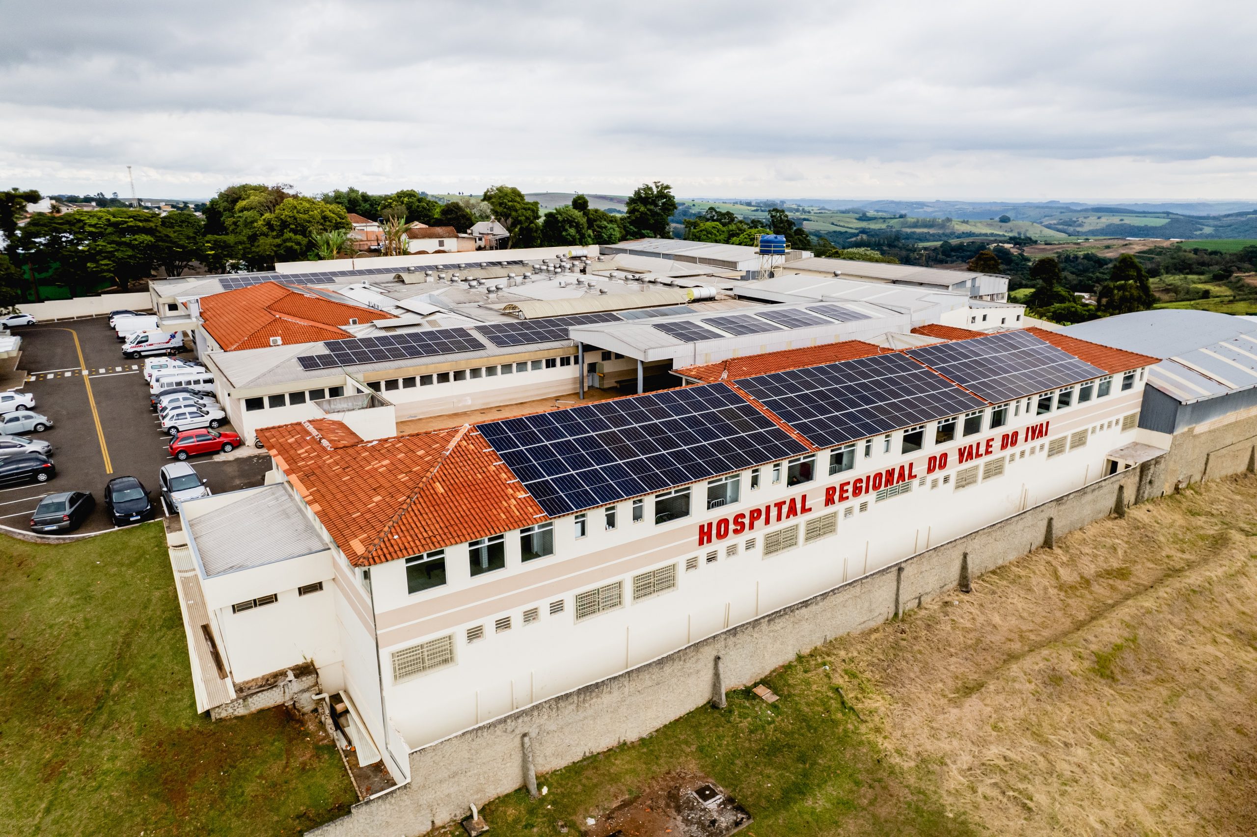 Imagem aérea de prédio baixo com placas fotovoltaicas sobre o telhado e na fachada escrito Hospital Regional do Vale do Ivaí