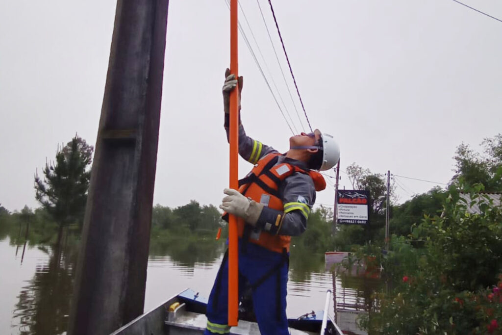 Eletricista com colete salva-vidas opera chave sobre barco em região alagada pelo Rio Iguaçu