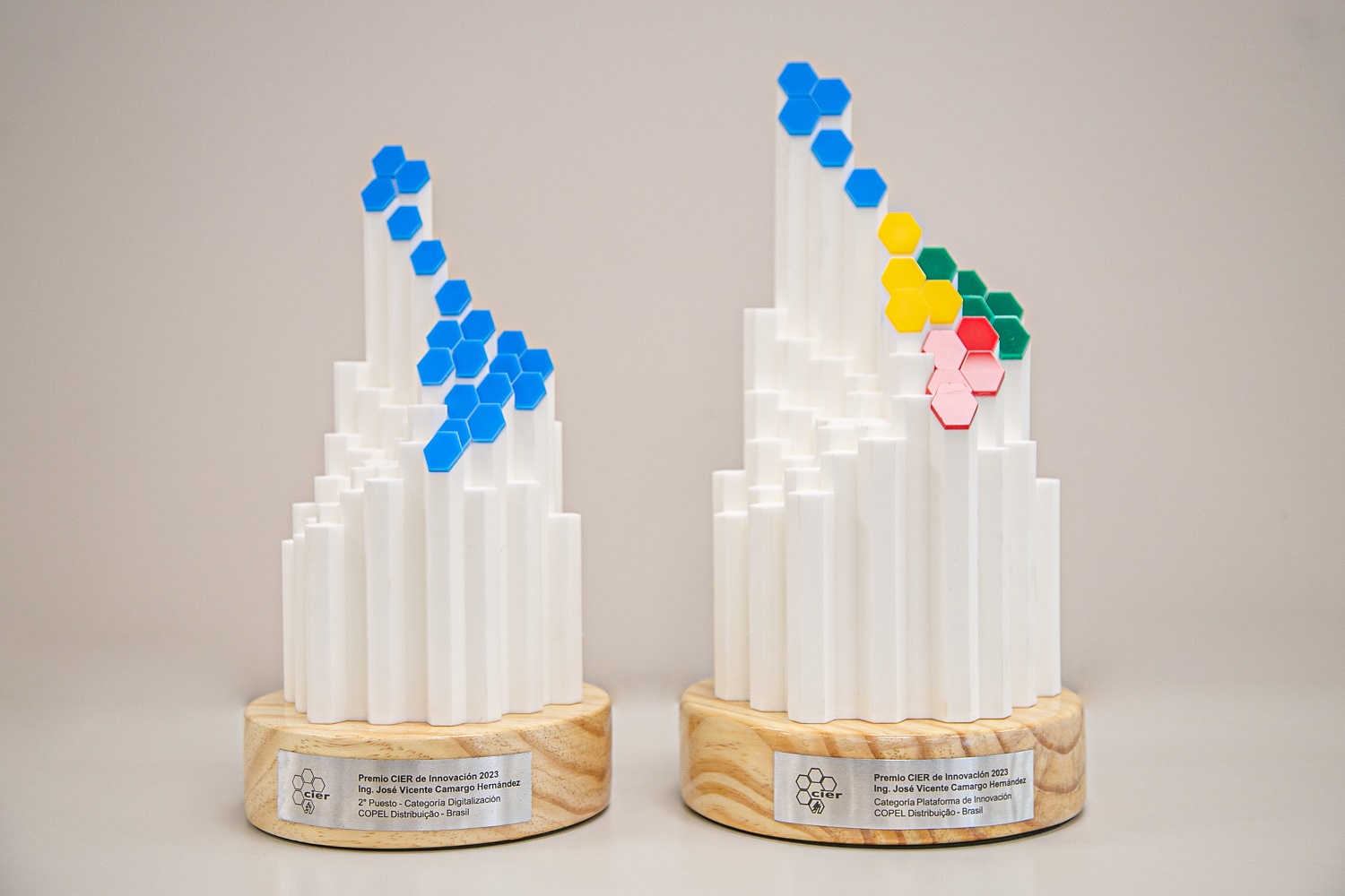 Troféus brancos com detalhes em azul, amarelo, verde e vermelho, em primeiro plano com fundo bege
