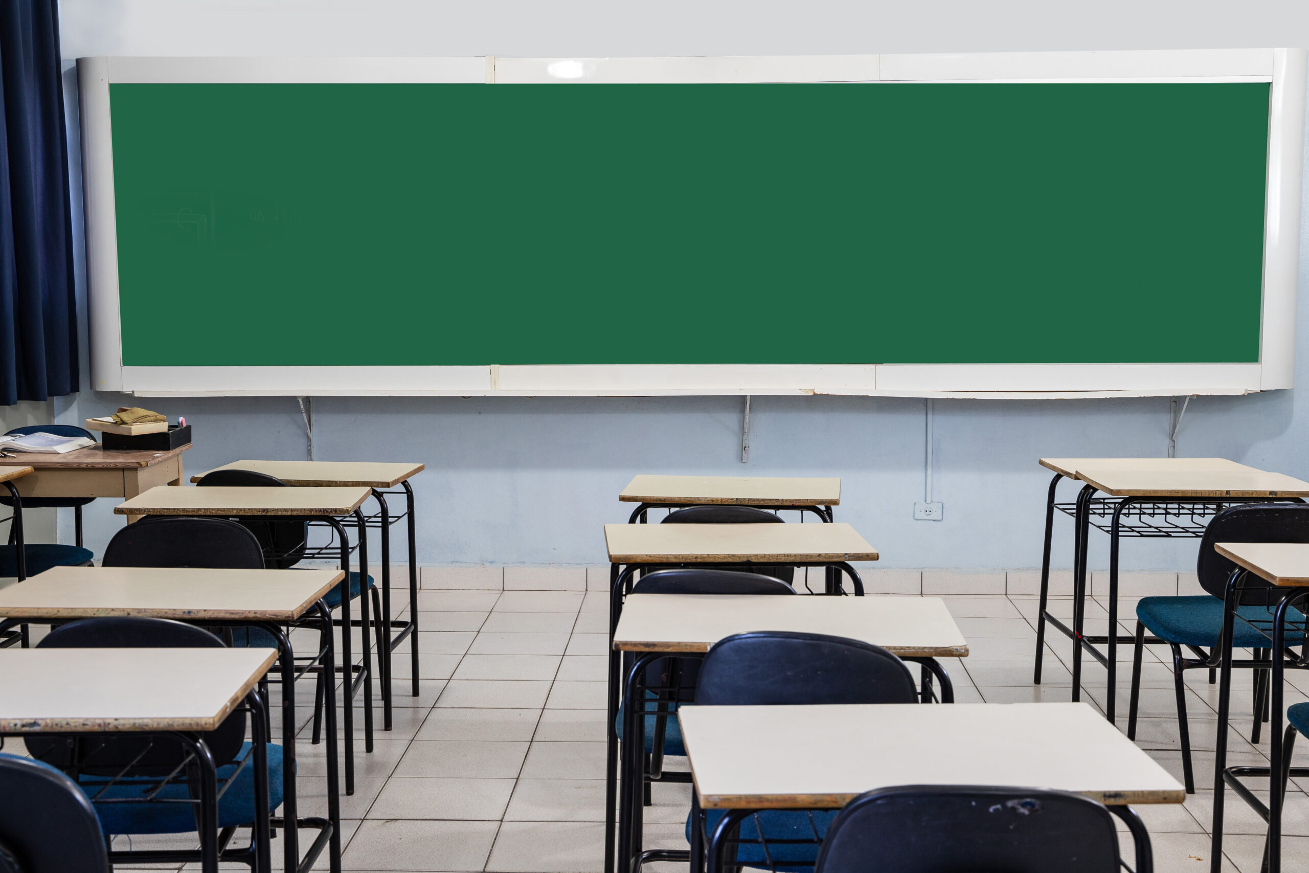 Sala de aula em plano médio, carteiras vazias e quadro verde