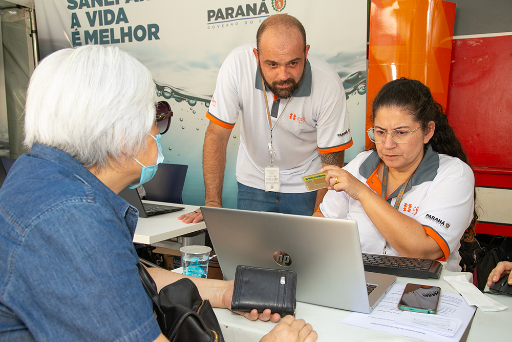 Atendentes uniformizados atendem consumidor que está sentado, de costas.