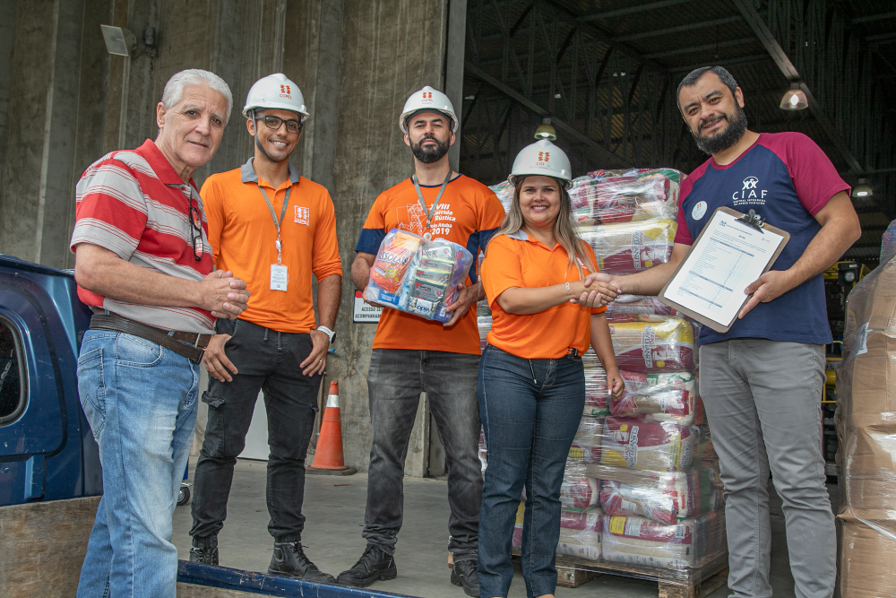 Cinco pessoas em pé, sendo três com camiseta laranja da Copel, junto a um palet de cestas básicas.