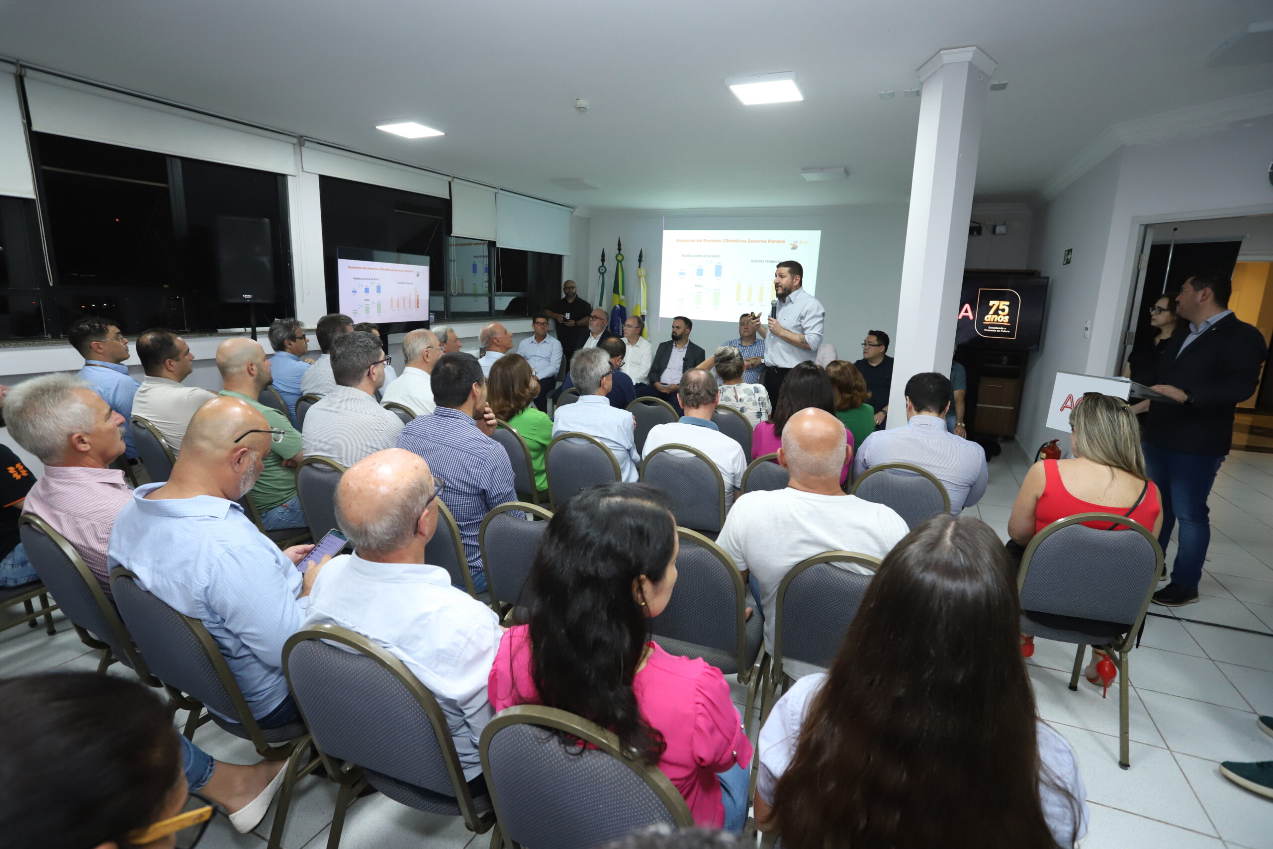 Auditório com pessoas sentadas de costas e, ao fundo, diretor da Copel em pé fazendo apresentação