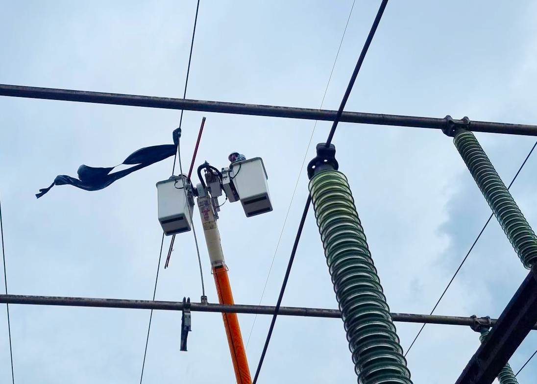 Equipe retira balão de linha de transmissão. Dois eletricistas sobre cesto aéreo