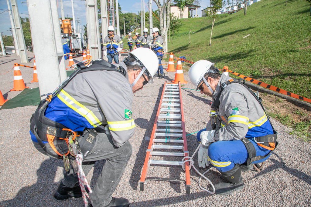 Alunos com uniforme de eletricistas treinam amarração em escada deitada no chão