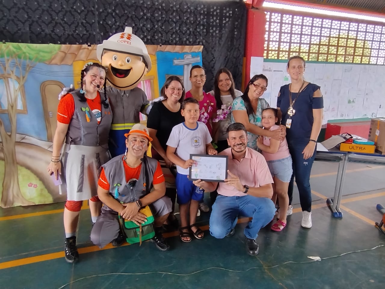 Pessoas sorridentes reunidas em entrega de um certificado em quadra de escola