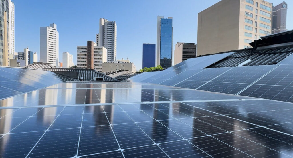 Visão aérea de placas solares com prédios ao fundo