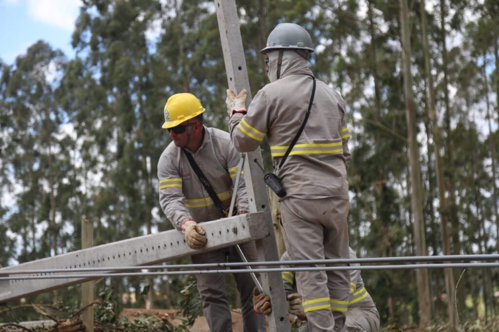 Eletricistas trabalham erguendo poste quebrado
